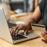 Hand of young African American female buyer with card ordering goods online