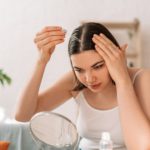Lady sitting on the couch looks in the mirror and drips hair oil with a pipette on her hair