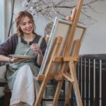 Young female artist works on abstract acrylic painting on canvas in art painting studio.