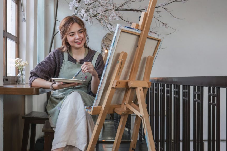 Young female artist works on abstract acrylic painting on canvas in art painting studio.