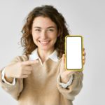 Young happy woman pointing at big mobile phone screen presenting new trendy app.