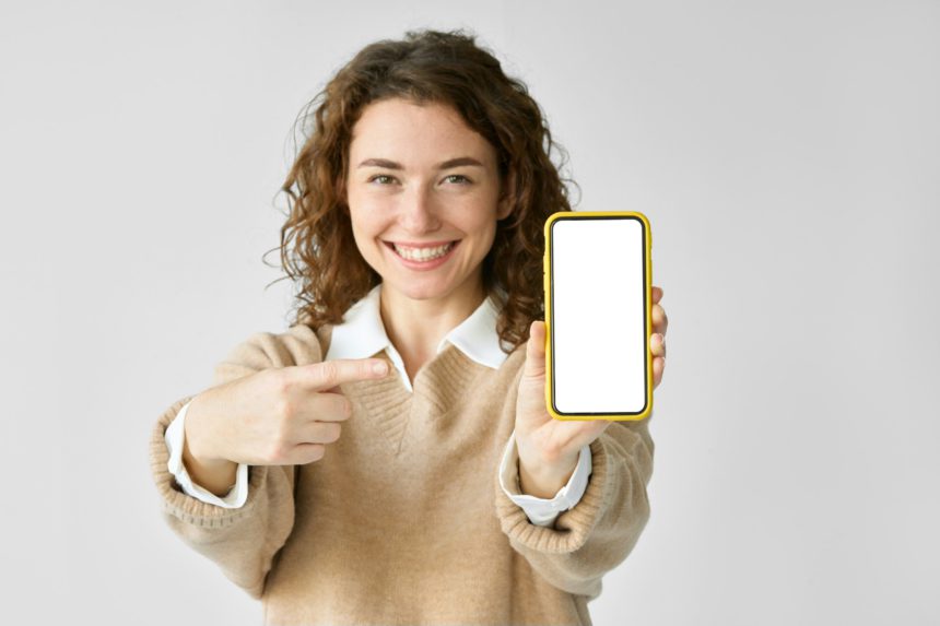 Young happy woman pointing at big mobile phone screen presenting new trendy app.